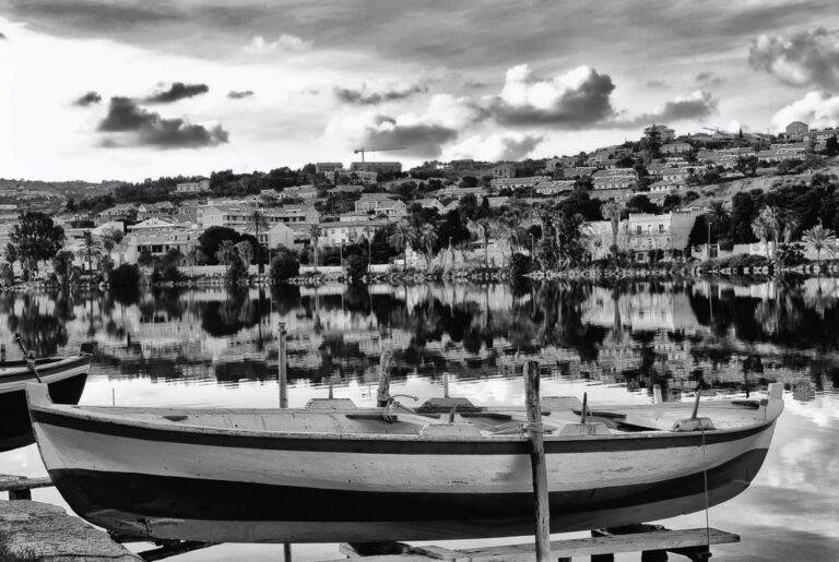 Ganzirri in bianco e nero: quieta figura della barca tra lago e città