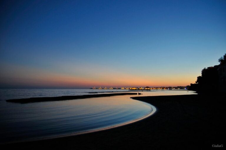 Tramonto sul mare: serenità e ritmo curvo della battigia tra luce fredda e riflessi dorati